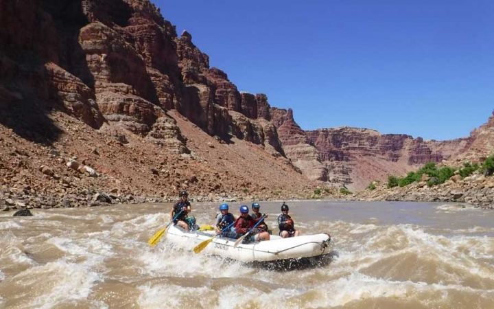 A group of students paddle a raft through whitewater.